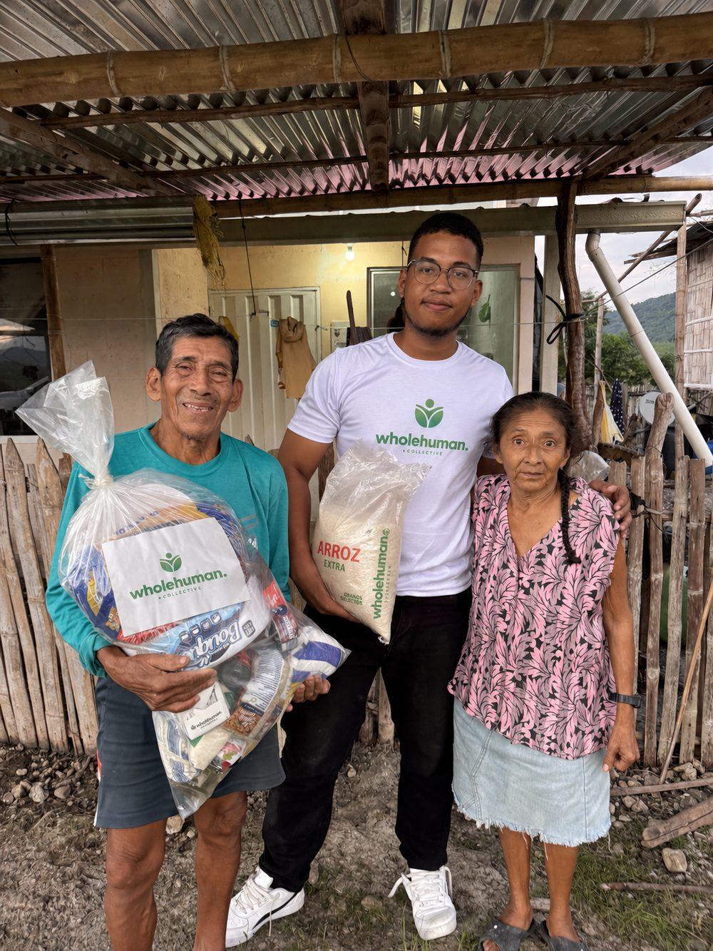 A Wholehuman team member with an older couple holding bags of food outside their home