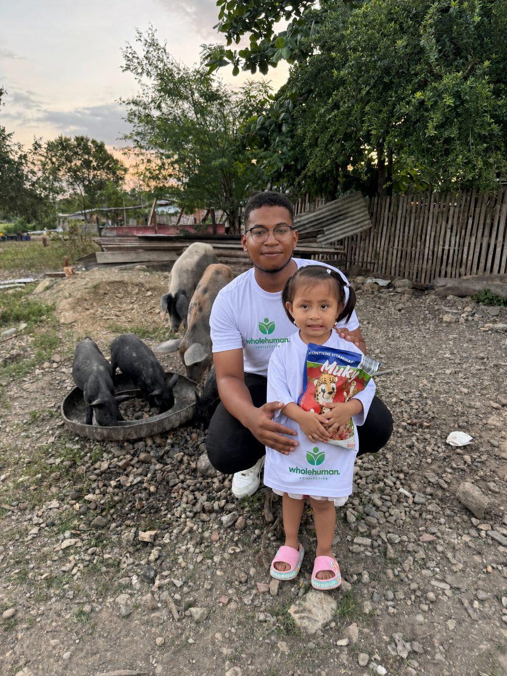 A Wholehuman team member kneeling beside a little girl holding a box of cereal in her family’s yard