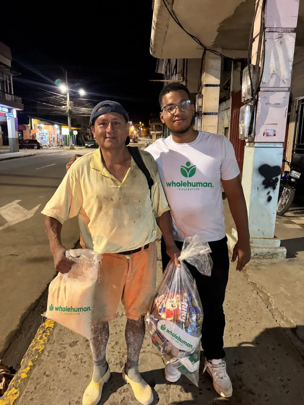 A Wholehuman team member and a man holding bags of food on a street at night